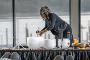 Photo of Angela of GlassWing Medicine playing frosted crystal bowls on a platform with a clear window behind her for an event