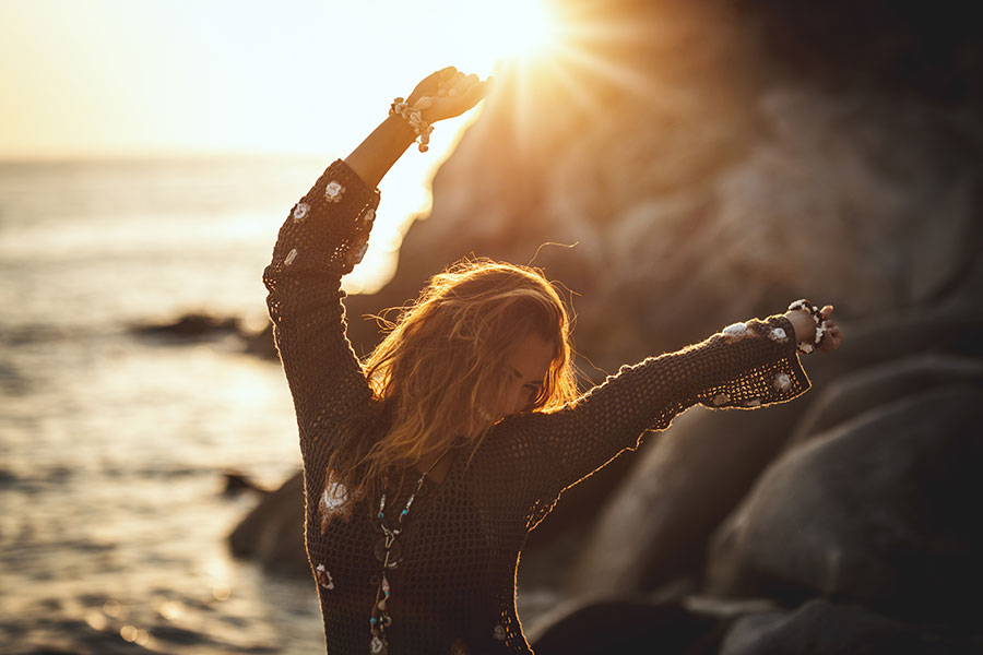 woman by the ocean happy and dancing in the sunset next to rocks - glasswing medicine onalaska, wa