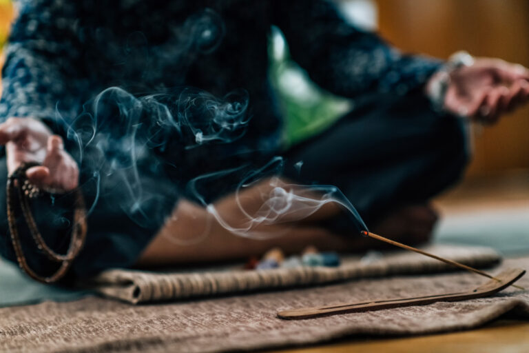 Image of a woman meditating with incense burning in front of her. Meditation Class at GlassWing Medicine