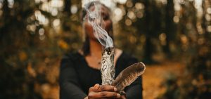 photo of glasswingmedicine holding a sage stick in the forest.