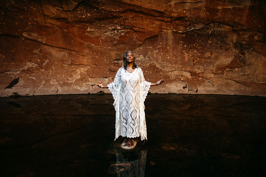 Angela of GlassWing Medicine in Sedona agains the redrocks in the middle of a river standing with arms stretched out Primal Voice
